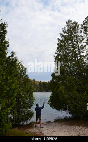 Un homme essaye la pêche à la mouche sur les rives d'un lac entre les deux arbres. Banque D'Images