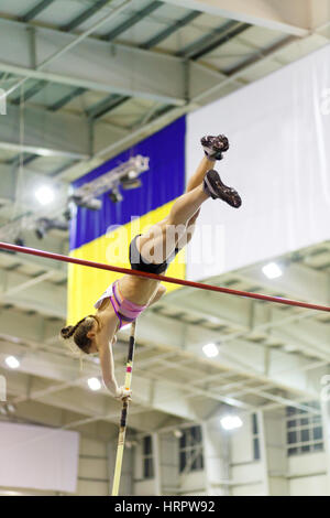 Jeune femme vaoulting bar plus athlétique avec mât contre drapeau sur la piste intérieure et championnat de champ Banque D'Images