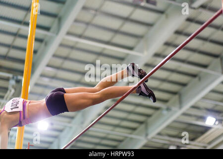 Jeune femme vaoulting bar plus athlétique avec mât contre drapeau sur la piste intérieure et championnat de champ Banque D'Images