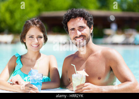 Heureux couple having cocktails dans la piscine Banque D'Images