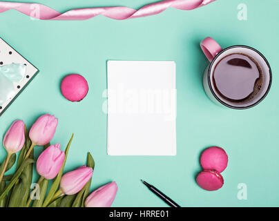 Papier blanc, tulipe rose, macarons et café dans un mug sur fond vert pastel Banque D'Images