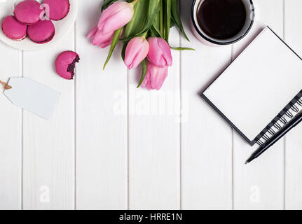 Tulipe rose, macarons, vide le bloc-notes et de café sur la table en bois blanc. Articles de printemps, vue du dessus Banque D'Images