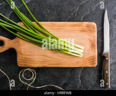 Un bouquet d'oignons verts sur une planche à découper. Fond noir ardoise. Banque D'Images