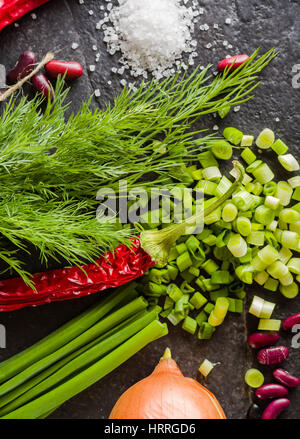 L'Arrangement de la ciboulette, des oignons, des haricots et de l'aneth sur un fond noir ardoise en pierre. Vue de dessus. Banque D'Images