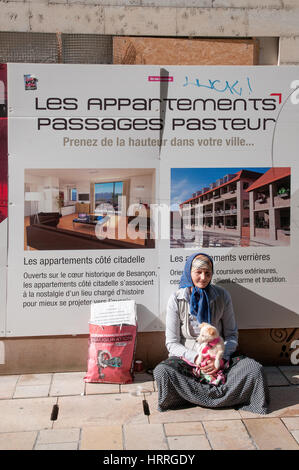 Jeune femme musulmane immigrants réfugiés avec petit chien chiot blanc la mendicité en face de l'affiche pour appartements de luxe à Besancon Banque D'Images