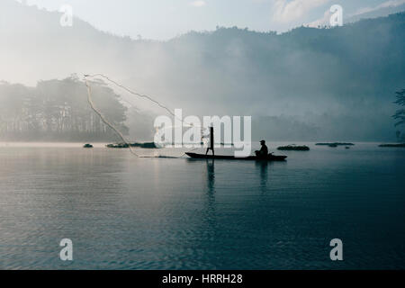 Le pêcheur son filet de pêche dans la rivière au début de la couleur bleu matin pour attraper des poissons à la pêche partenaire qui dirige le bateau. Banque D'Images