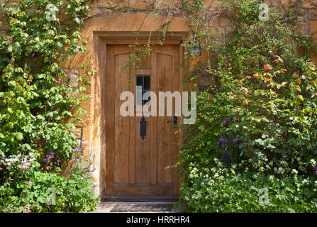 Portes en bois brun dans une vieille maison en pierre de chaux anglais traditionnel avec des fleurs, rosier, escalade des arbustes dans le jardin de devant, sur la journée d'été . Banque D'Images