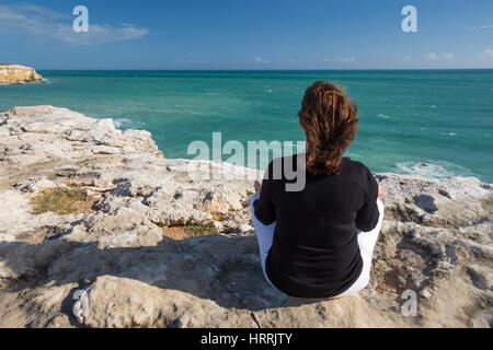 WOMAN MEDITATING ON CLIFF TOP EN POSITION DE YOGA FACE À LA MER Cabo Rojo, PUERTO RICO Banque D'Images