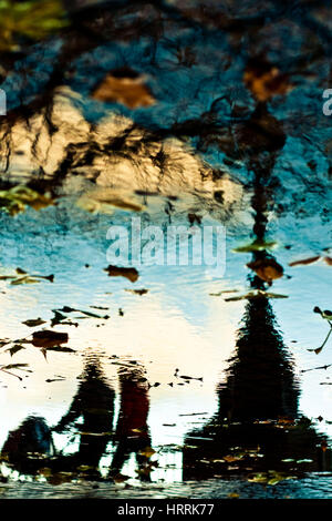 Silhouettes de quelques personnes reflètent dans l'eau au cours de jour de pluie dans la ville Banque D'Images