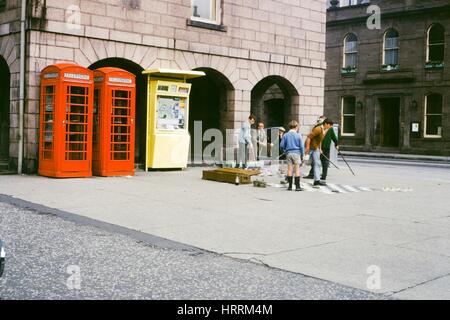 Un groupe d'hommes et de jeunes garçons jouer aux dames sur de grands panneaux et vous détendre dans une place publique, avec deux cabines téléphoniques traditionnels britanniques visible, Royaume-Uni, 1970. Banque D'Images