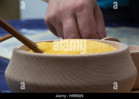 La farine de maïs dans le bol en bois avec cuillère sur la table d'accueil. Dans l'arrière-plan les mains de pâte filo préparation pour gâteau au fromage Banque D'Images