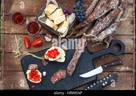 Du vin et des hors-jeu. Pain, saucisse de viande de porc salés à sec, tomate sur rustique en servant de sélection et le vin rouge dans le verre sur fond rustique, top v Banque D'Images