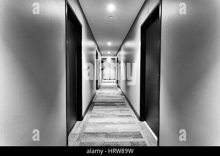 Corridor symétrique dans tout nouvel hôtel moderne avec la porte de chambre sur les côtés et des murs blancs éclairés par les lumières vives. Pas de clients en vue. Banque D'Images