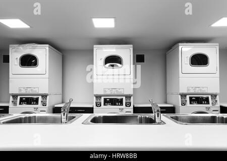 Ligne de self-service grand lave-linge et sèche-linge et la lessive à côté de lavabos et robinets d'eau de table en attente de clients Banque D'Images