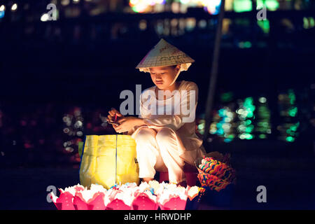 Hoi An, Vietnam - Mars 14, 2014 : fille vietnamienne en chapeau conique de vendre des bougies pour les touristes dans la nuit. Banque D'Images