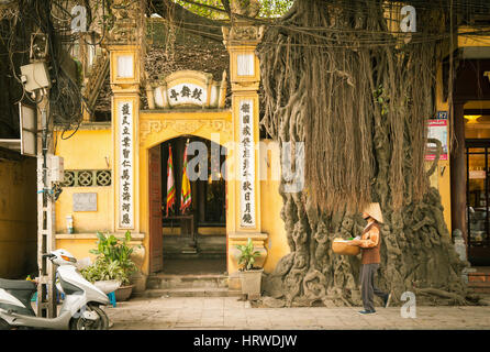 Hanoi, Vietnam - 25 Avril 2014 : dans la région de chapeau conique avec panier en mains est en passant par le temple de la rue du vieux quartier de Hanoi, Vi Banque D'Images