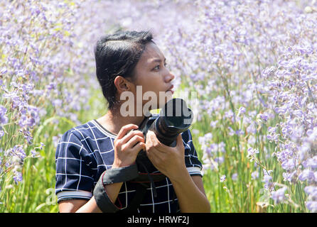 Femme avec un appareil photo du milieu de la prairie avec fleurs violettes Murdannia giganteum. Photographe à la nature. Banque D'Images