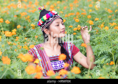 Femme Asiatique en costume traditionnel pour Karen renifle une fleur orange Cosmos on meadow Banque D'Images