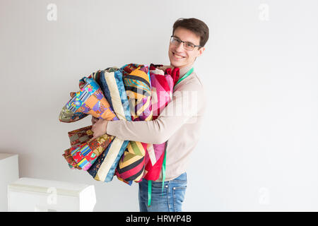 Beau jeune homme tailleur tenant une pile de couleurs patchwork quilts pliés sur un fond blanc. De nombreuses couvertures en patchwork coloré de style dans l'h Banque D'Images