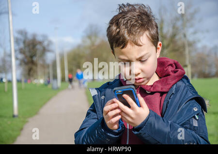 Un jeune garçon joue Pokemon rendez sur un téléphone mobile à l'extérieur dans le parc. Banque D'Images