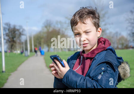 Un jeune garçon joue Pokemon rendez sur un téléphone mobile à l'extérieur dans le parc. Banque D'Images