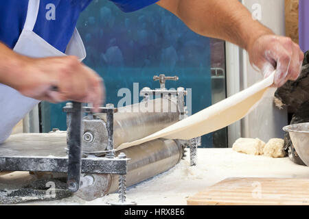 Les hommes mains abaisser la pâte de près. L'homme préparer la pâte pour la cuisson des pâtes sur une table en bois dans la région de cafe Banque D'Images