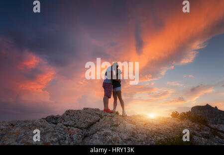 Silhouettes d'embrasser un homme et femme sur le sommet de la montagne au coucher du soleil. Paysage avec silhouette de jeunes contre ciel coloré Banque D'Images