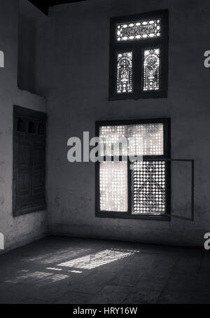 Old abandoned dark endommagé chambre sale avec deux cassé des fenêtres ornées de bois couverts par la grille en bois entrelacé (mashrabiya). Tourné en noir et blanc Banque D'Images