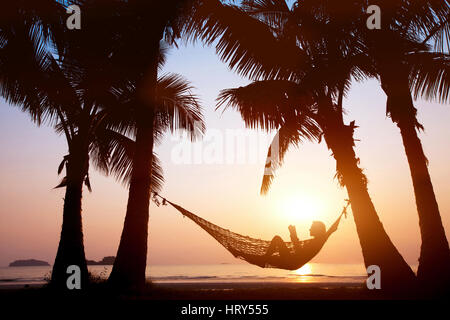 Woman relaxing in hammock sur beau coucher de soleil sur la plage, maison de vacances concept Banque D'Images