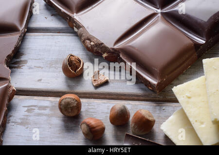 Morceaux de chocolat, tuile de noix et graines de cacao sur fond de bois Banque D'Images