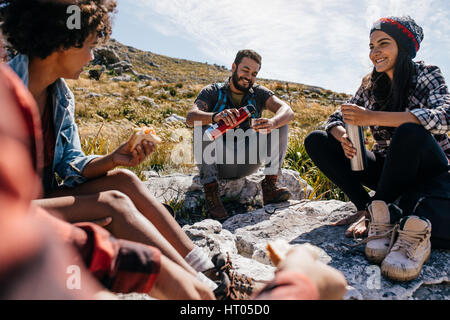 Groupe de randonneurs couple eating sandwiches et de boire du café tout en vous relaxant dans le champ. Les jeunes ayant un repos au cours de pays randonnée. Banque D'Images