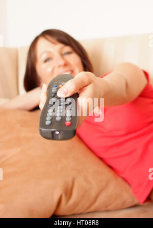 Junge Frau mit Fernbedienung liegt auf Couch - young woman with remote control on couch Banque D'Images