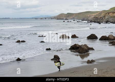 Un surfeur à marcher le long de la rive, tenant une planche de surf. Banque D'Images