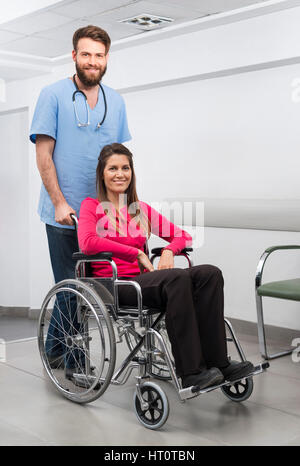 Portrait of smiling female patient assis en fauteuil roulant alors qu'infirmier debout derrière à l'hôpital Banque D'Images