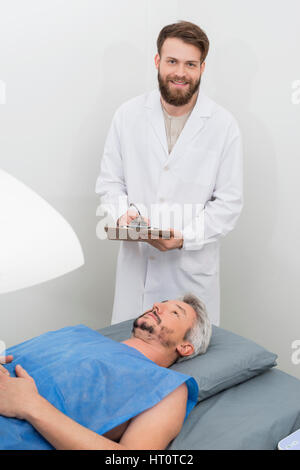 Portrait of male doctor writing on clipboard tandis que l'homme mature subissant la densitométrie osseuse à l'hôpital d'examen Banque D'Images