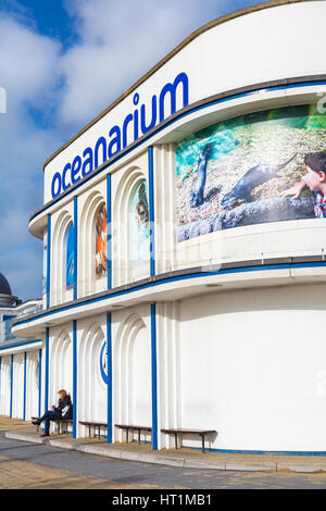 Femme assise sur un banc à l'extérieur de l'Oceanarium, le Bournemouth aquarium, le soleil brille, à Bournemouth, Dorset, UK en Mars Banque D'Images