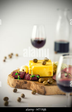 Vin rouge, assiette de fromage au salami et olives vertes sur fond blanc, jaune l'emmental sur plateau de fromages en bois vintage. Deux verres à vin rouge. Banque D'Images