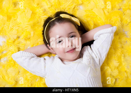 Heureux confiant girl laying on une plume jaune - printemps/Pâques prop Banque D'Images