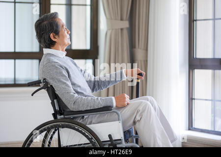 Senior man sitting in wheelchair et looking out window Banque D'Images