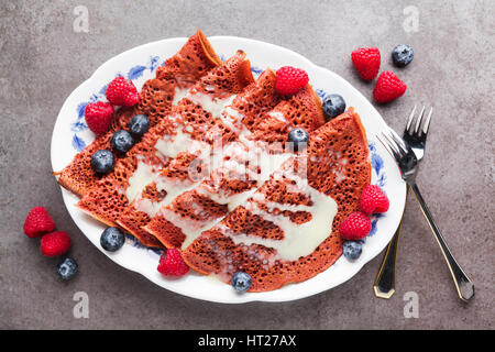 Matin le velours rouge des crêpes sur une plaque recouverte de crème vanille, framboises et bleuets. Petit-déjeuner sain Banque D'Images