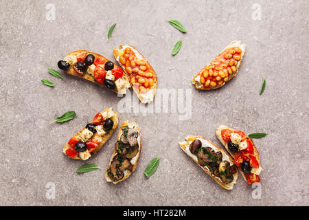 Variété de petites bruschetta avec salade caprese , haricots blancs sur la grille avec de la sauce tomate et champignons frits avec du fromage doux, servi sur le dos gris Banque D'Images