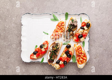 Variété de petites bruschetta avec salade caprese , haricots blancs sur la grille avec de la sauce tomate et champignons frits avec du fromage doux, servi sur le dos gris Banque D'Images