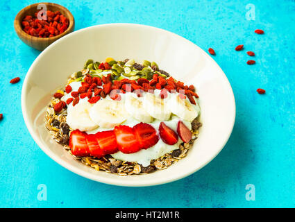 Bol de muesli avec les baies de goji, fraises, yogourt et des tranches de banane, les graines de citrouille Banque D'Images