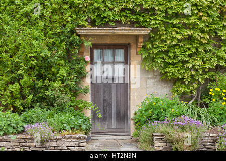 Vieilles portes en bois brun en anglais maison en pierre avec des fleurs dans le jardin de devant, entouré de grimpeur . Banque D'Images