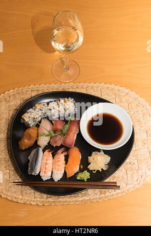 Repas sushis sur une plaque noire avec un verre de vin blanc sur une table Banque D'Images