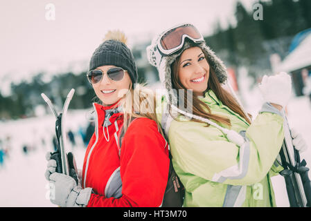 Belle jeune femme bénéficiant d'amis en vacances d'hiver. Ils debout avec des skis et à la recherche à l'appareil photo avec sourire. Banque D'Images