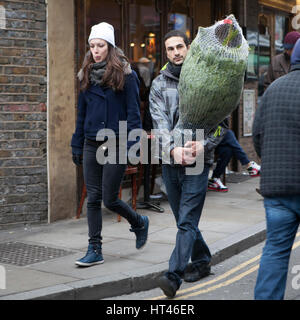 Londres, ANGLETERRE - 12 Décembre 2016 Un homme a acheté un arbre de Noël sur le marché aux fleurs de la Colombie-Britannique Banque D'Images