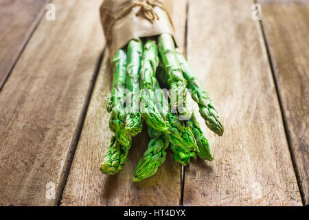 Ensemble de matières organiques fraîches vert asperges attachées avec de la ficelle sur la table de cuisine en bois en planches dans le rétroéclairage, closeup Banque D'Images