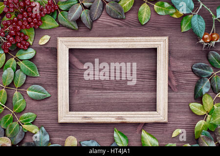 Cadre en bois vide sur une surface marron entre les feuilles et fruits rouges du viburnum Banque D'Images