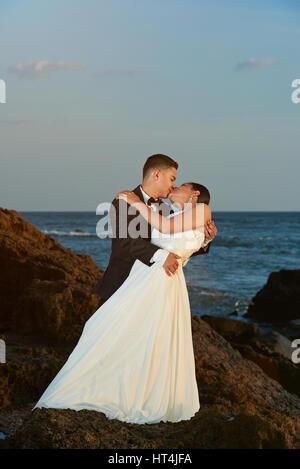 Mariée et le marié, baiser sur le coucher du soleil la lumière. Maintenez l'homme femme et de l'embrasser sur la côte rocheuse Banque D'Images